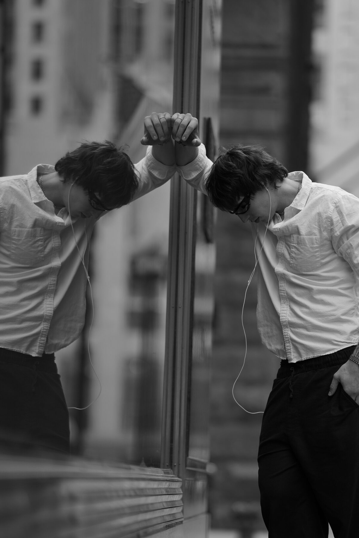 Sotos rests his forehead against a storefront window, eyes down — a quiet, off-stage moment between performances.