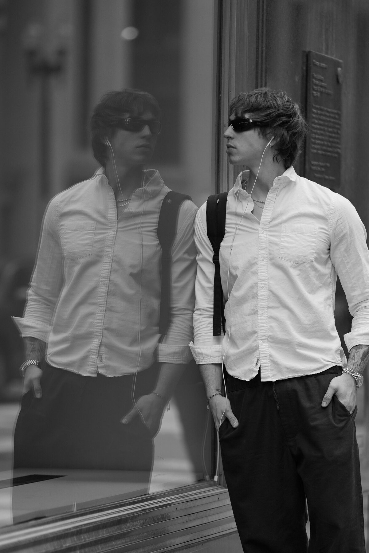 A B&W image of Sotos in sunglasses leaning into a storefront window, his reflection visible alongside him — two of him in the same frame.