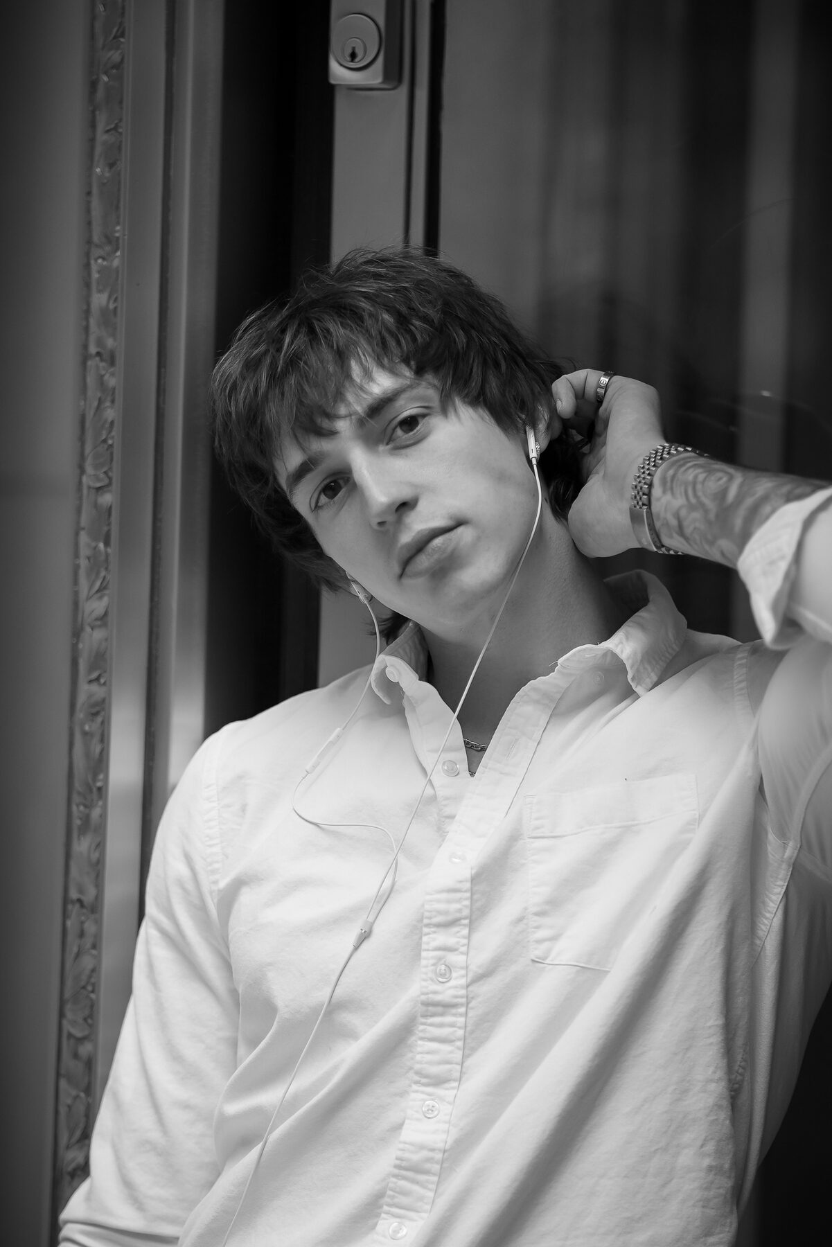 A close B&W portrait of Sotos, hand near his neck, eyes lifted to the camera — quiet, unguarded.