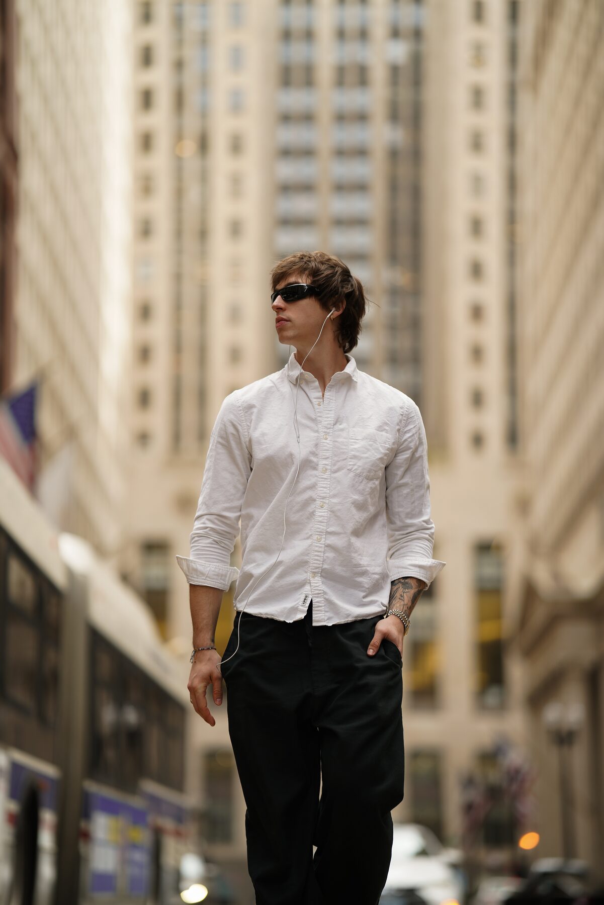 Sotos walking forward through a Chicago urban canyon at street level, sunglasses on, building toward the next thing.